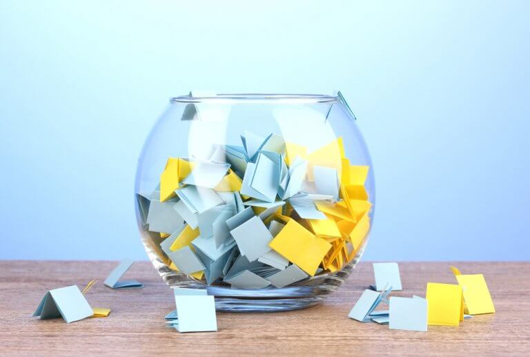 Pieces-of-paper-for-lottery-in-vase-on-wooden-table-on-blue-background
